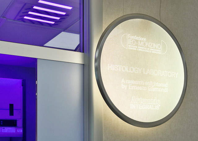 Fondazione IEO-Monzino Histology Laboratory entrance with illuminated circular Artemide sign and purple ceiling lights.