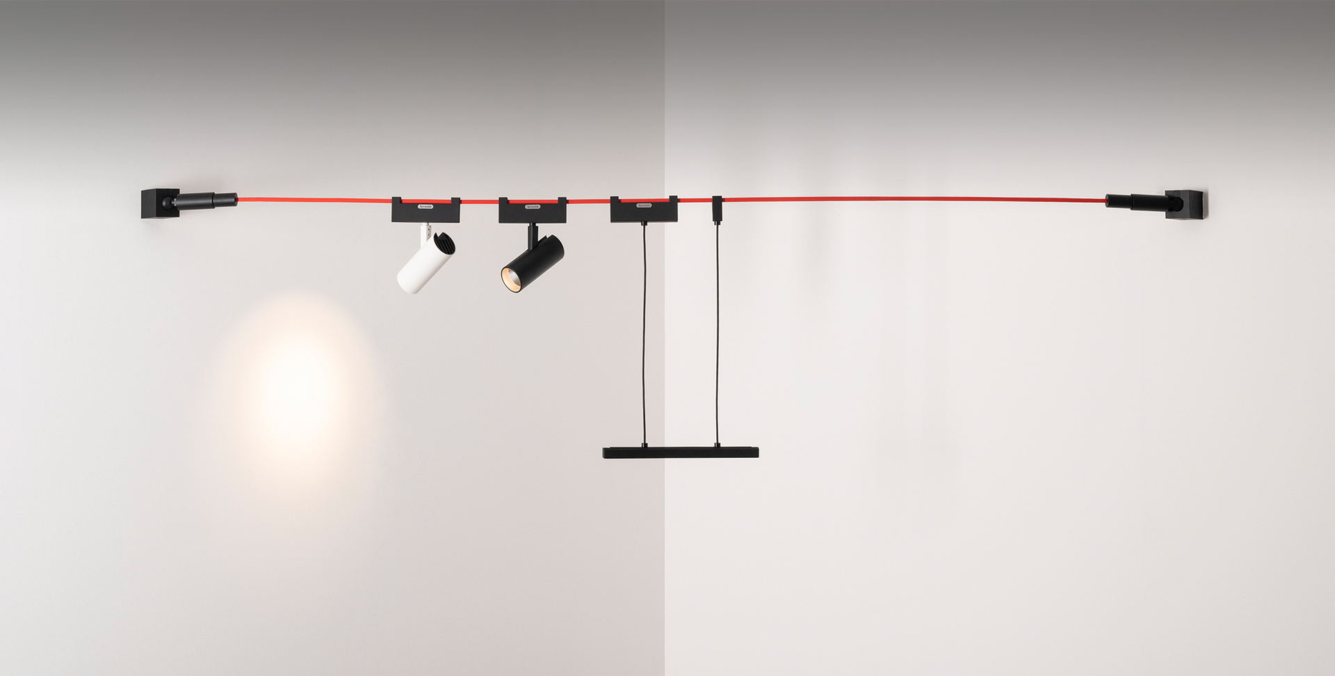Sistema a binario a parete Artemide con cavo rosso, due faretti neri orientabili, un faretto bianco e una barra a sospensione.