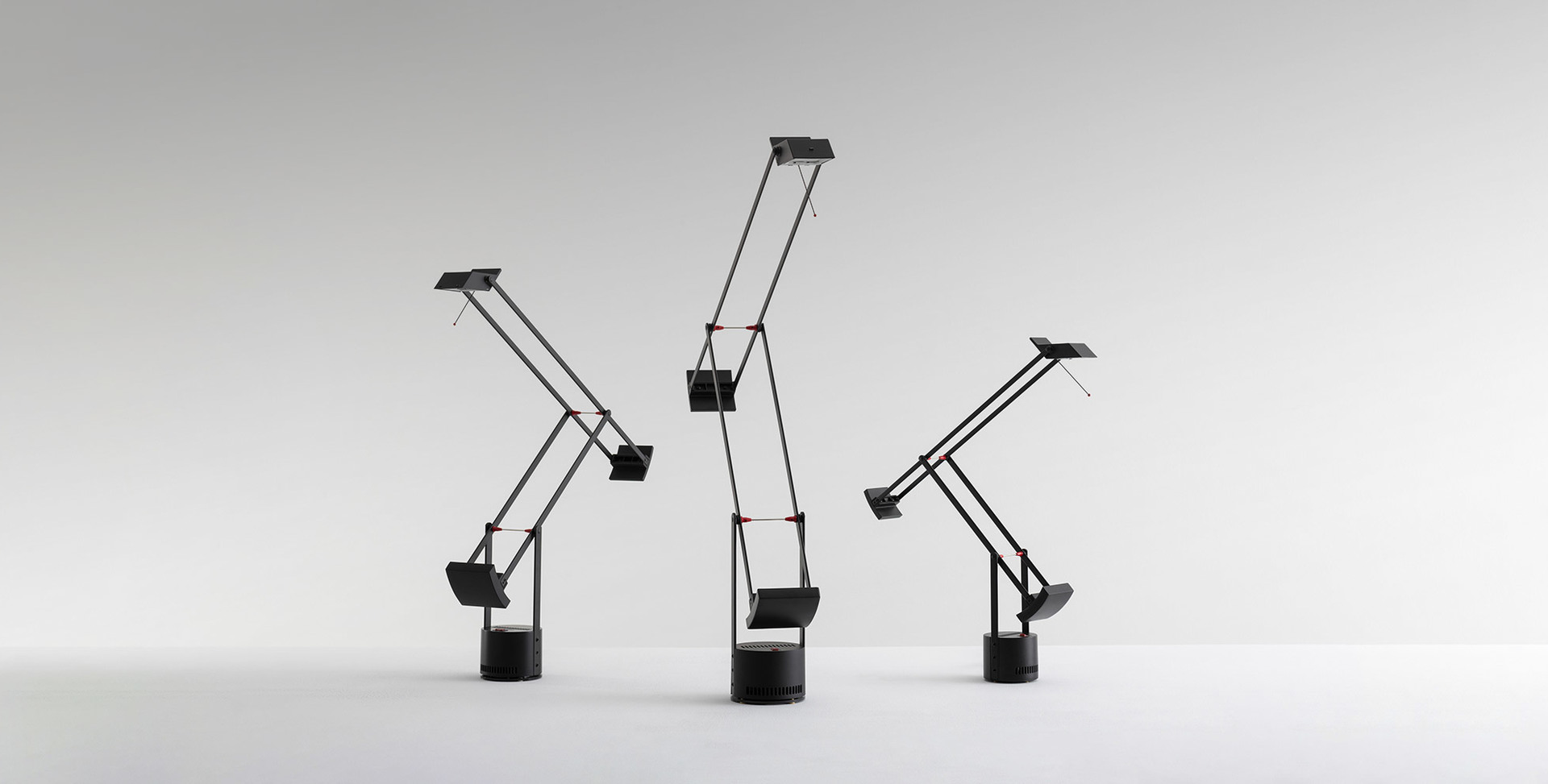 Three Artemide Tizio black desk lamps in different positions, showcasing their iconic counterbalance arm design on cylindrical bases
