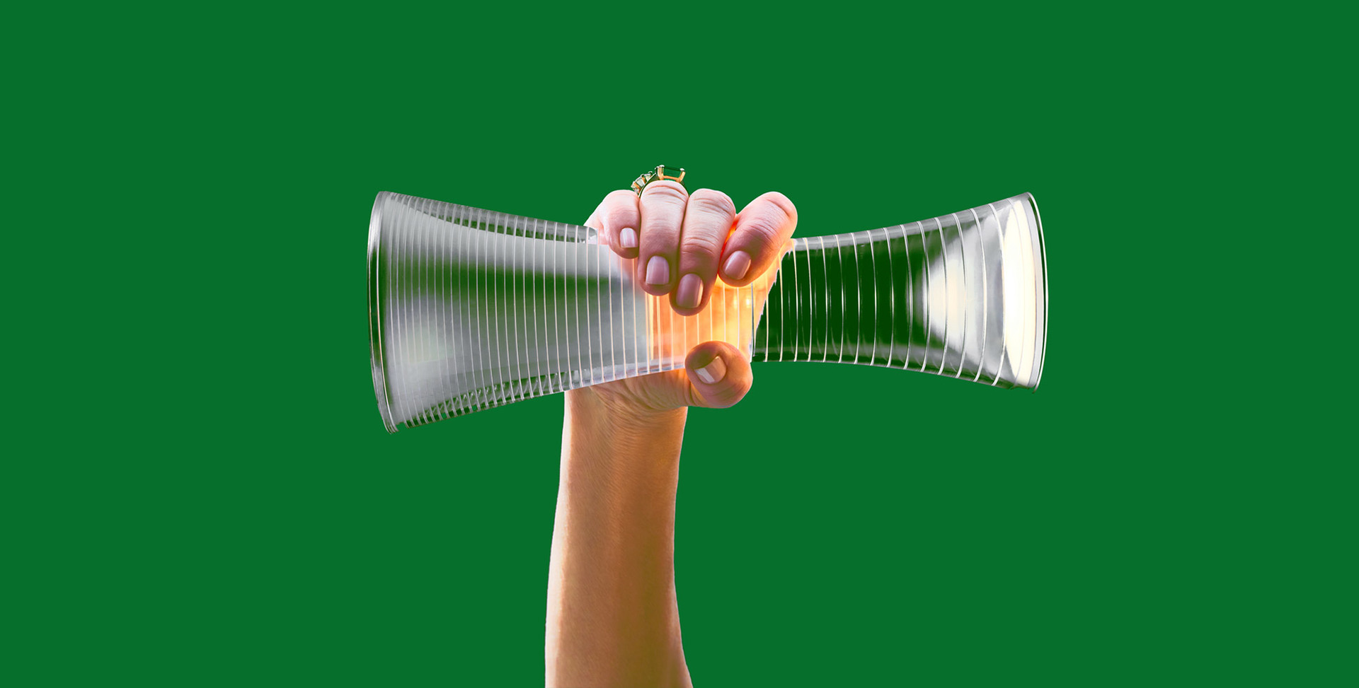 Mano che regge un diffusore in vetro nervato a forma di clessidra con luce calda, su sfondo verde