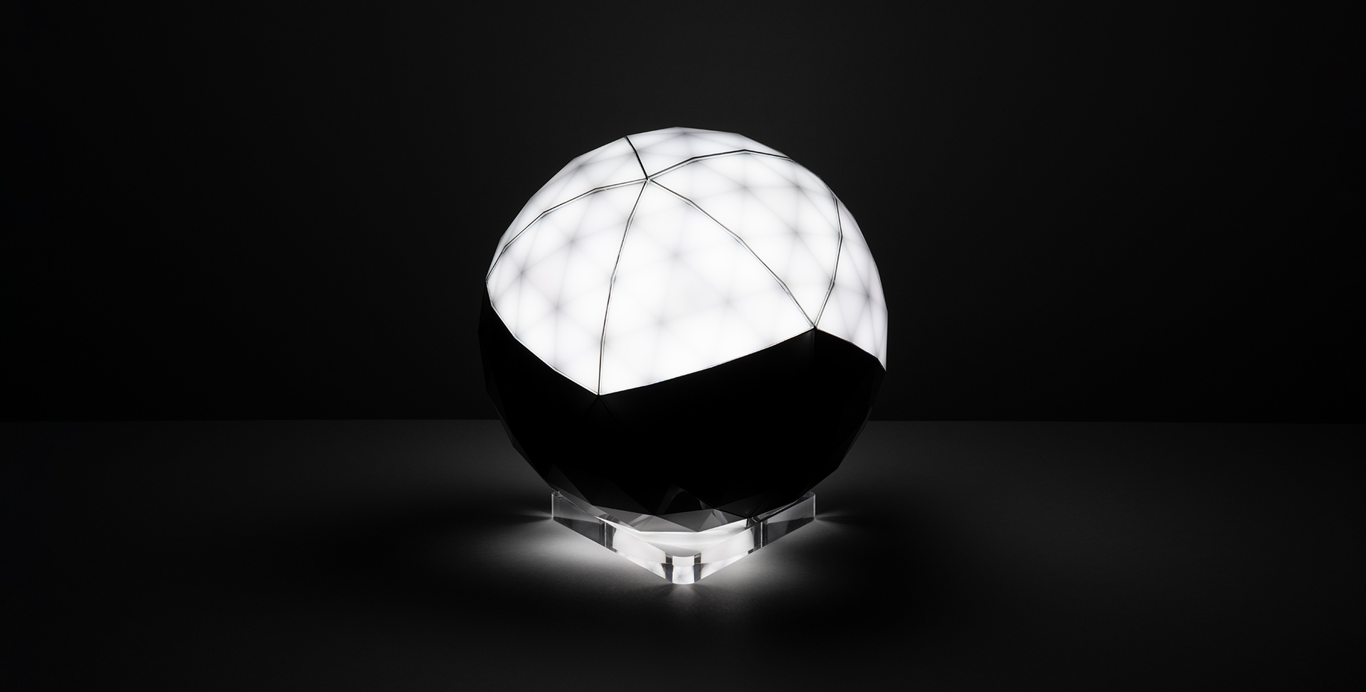 Lampada da tavolo sferica Artemide con metà superiore luminosa bianca segmentata, metà inferiore scura, su base in acrilico trasparente