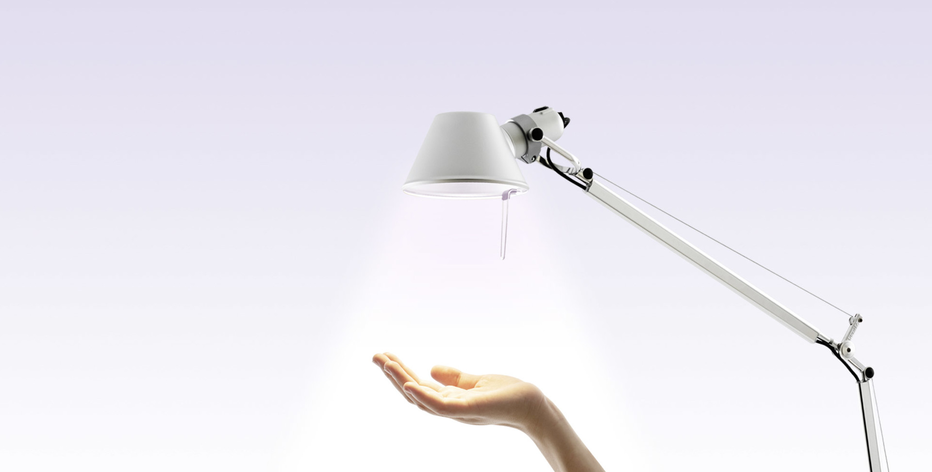 Lampada da tavolo Artemide Tolomeo bianca, con braccio articolato, che proietta luce calda su una mano aperta sottostante.