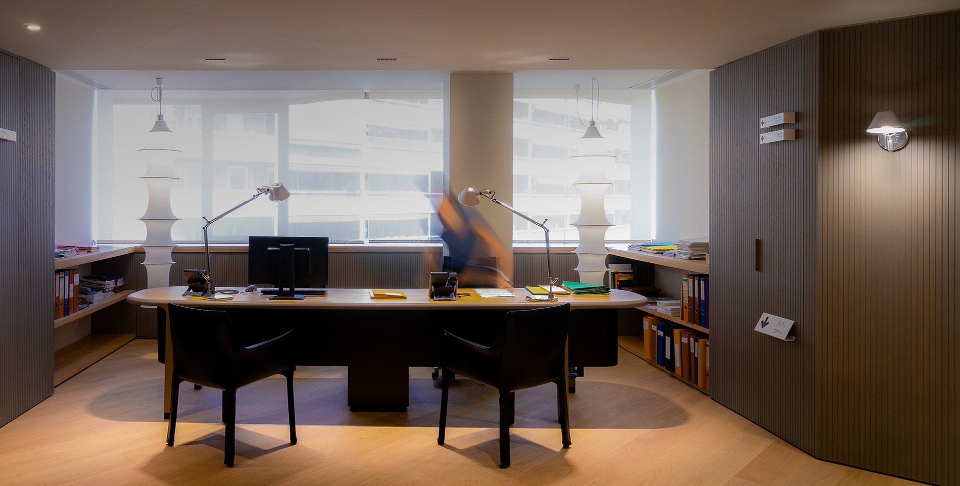 Ufficio moderno con scrivania curva, due lampade da tavolo Artemide Tolomeo, lampade a sospensione e applique su pannello scanalato.
