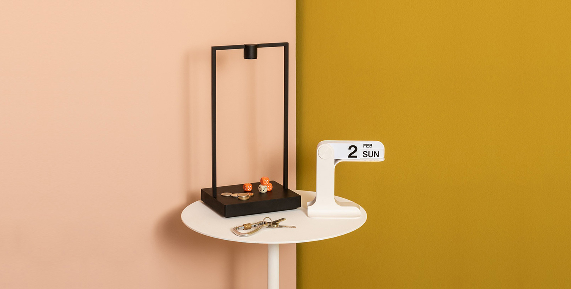 Lampada da tavolo rettangolare nera con struttura minimalista su tavolino bianco, abbinata a piccoli oggetti decorativi e un calendario con domenica 2 febbraio