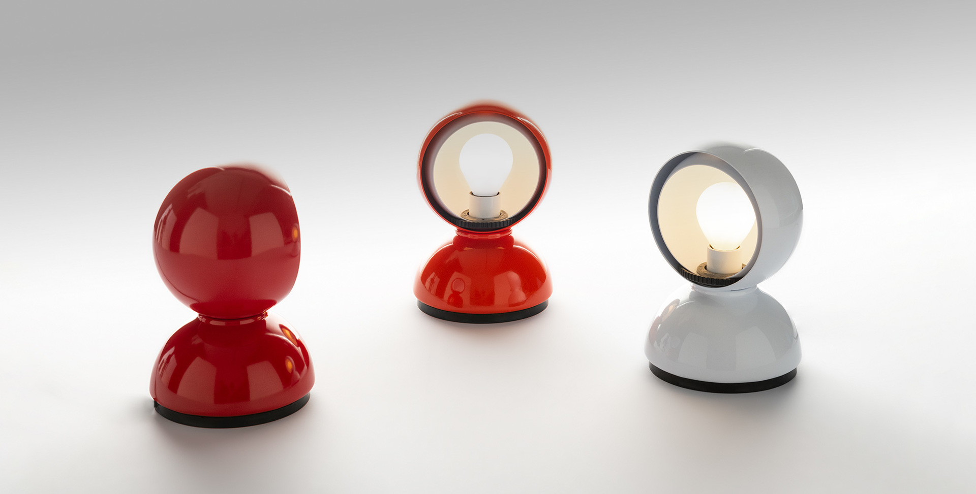 Three Artemide Eclisse table lamps: two in red and one in white, with rotating spherical shades revealing the bulb inside