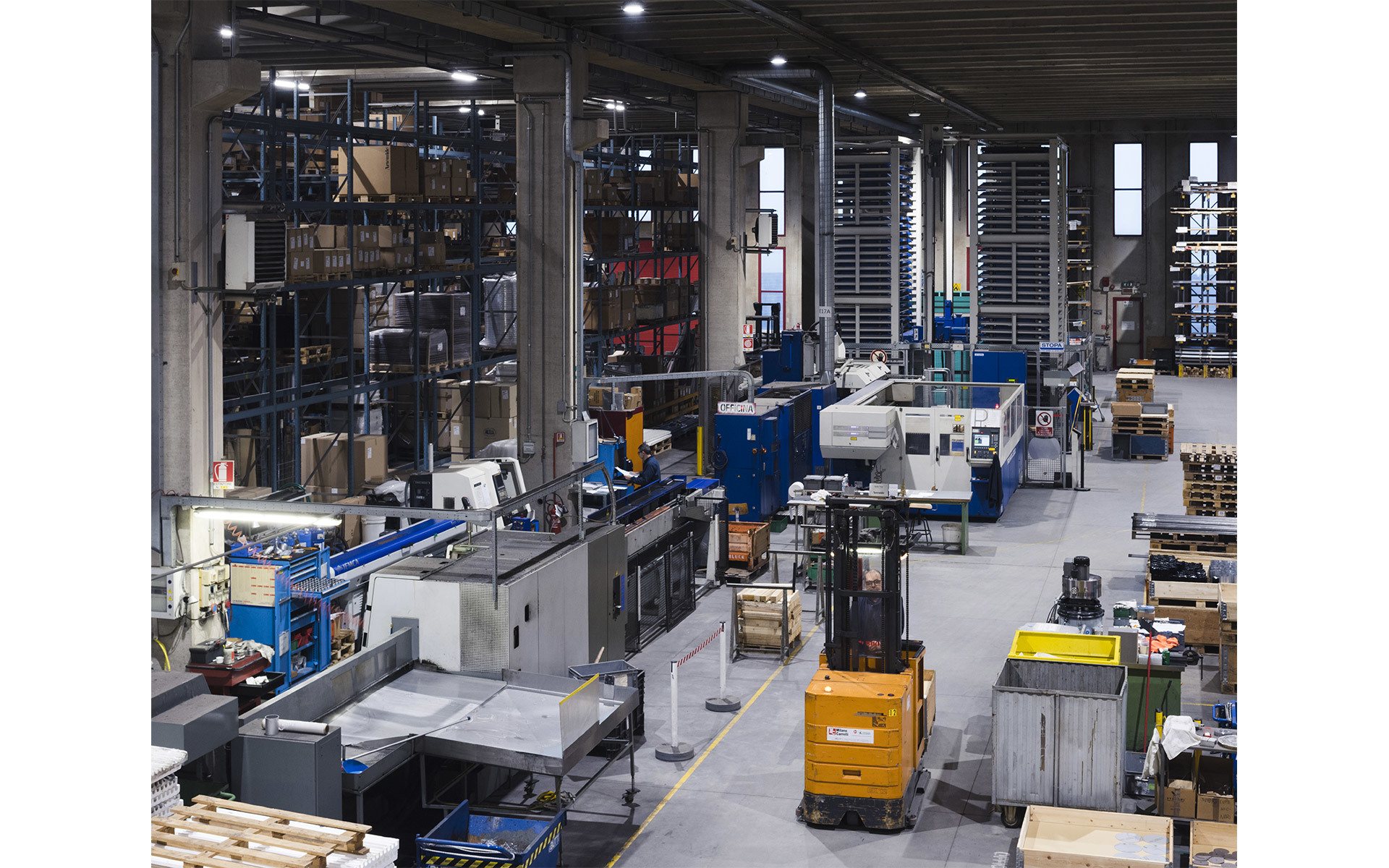 Grande stabilimento industriale con macchinari, sistemi di stoccaggio automatizzati, un carrello elevatore e illuminazione a soffitto.