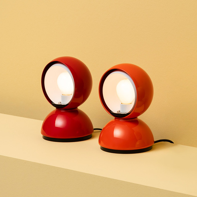 Two Artemide Eclisse table lamps in red, with rotatable spherical shades on dome bases, displayed on a shelf.
