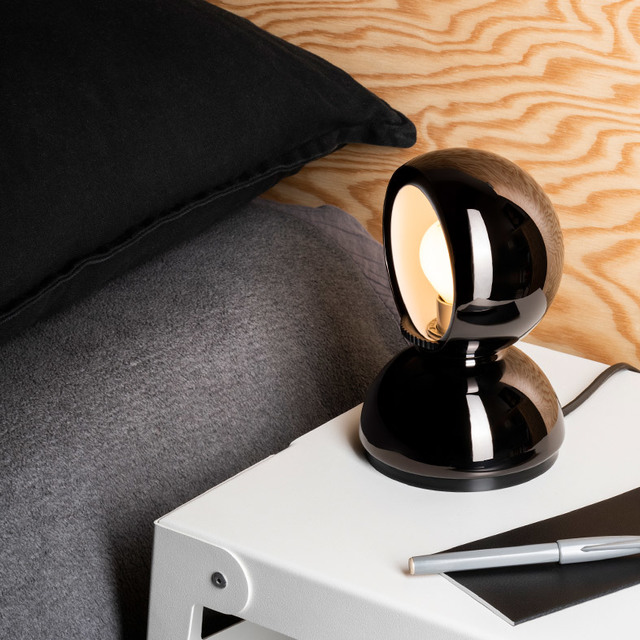 Artemide Eclisse table lamp in glossy black, spherical design with rotating shade, placed on a white bedside table.