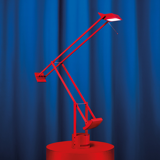 Artemide Tizio red desk lamp with articulated arm and counterweight, displayed on a red base against a blue background