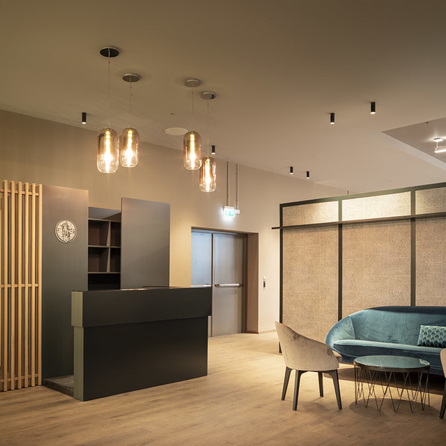 Area reception moderna con lampade a sospensione in vetro ambrato sopra una scrivania scura, faretti a soffitto sottili e un divano verde acqua in un angolo lounge.