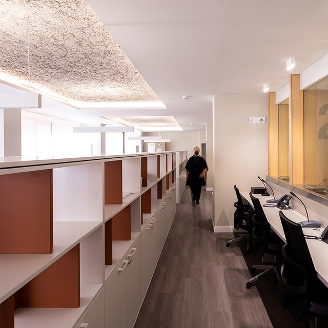 Corridoio di ufficio moderno con luci a soffitto incassate e pannelli texturizzati che illuminano postazioni di lavoro e una reception su entrambi i lati.