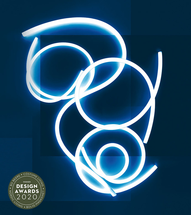Tubo LED flessibile Artemide attorcigliato in curve e spirali fluenti, luminoso bianco-blu su sfondo scuro. Vincitore Design Awards 2020.