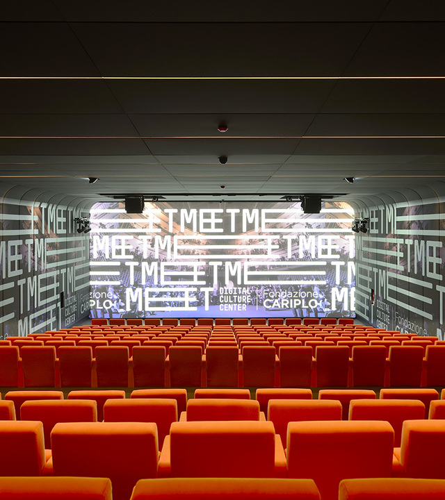 Auditorium with rows of red seats facing a large projection screen, with recessed ceiling lighting illuminating the space.