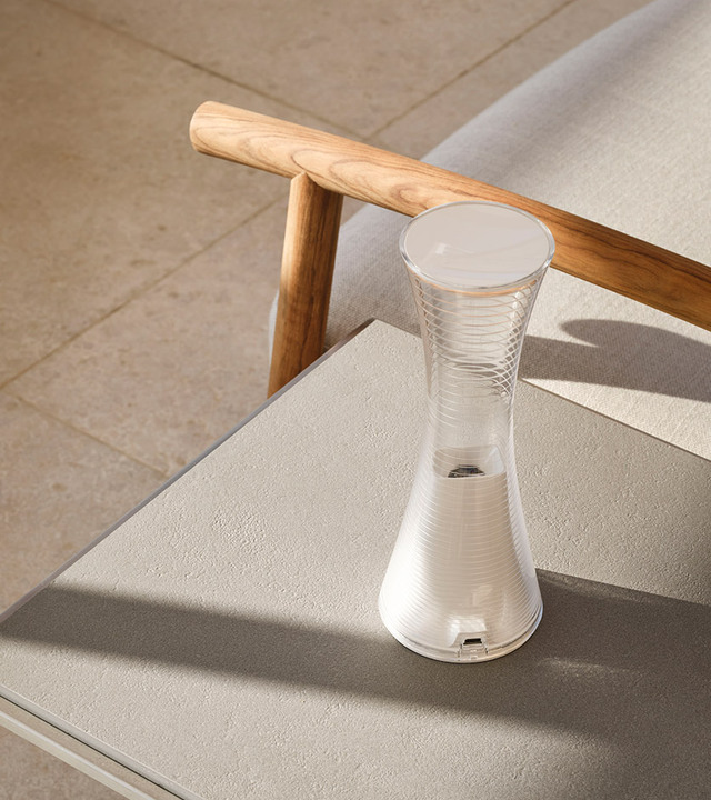 Lampada da tavolo portatile Artemide con corpo bianco nervato a forma di clessidra e diffusore superiore opaco, su tavolino da esterno
