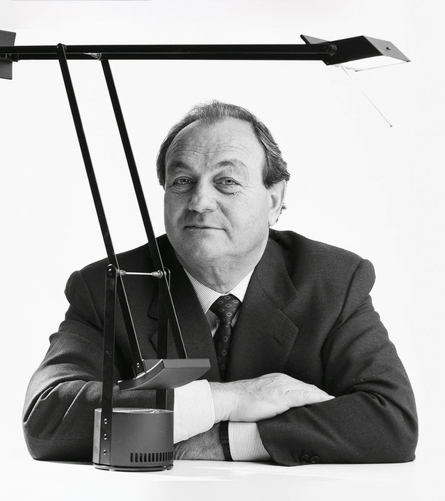 Man in suit posing with an Artemide Tizio desk lamp, a iconic black adjustable task light with counterbalance arm system.
