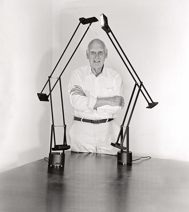 Man posing behind two black Tizio desk lamps by Artemide, their articulated arms forming a house shape on a table
