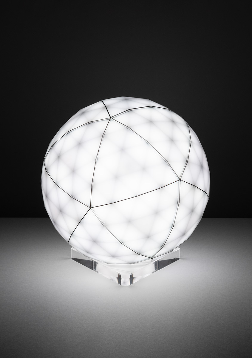 Lampada da tavolo sferica Artemide con diffusore bianco, motivo geometrico a fili neri, luce uniforme, su base in cristallo trasparente.