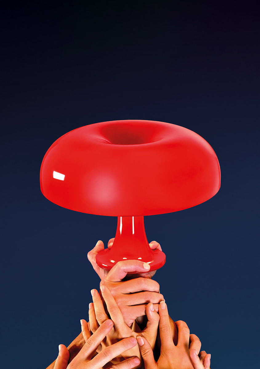 Più mani che si alzano insieme per reggere la lampada da tavolo Artemide Nessino con il suo iconico paralume rosso a fungo.