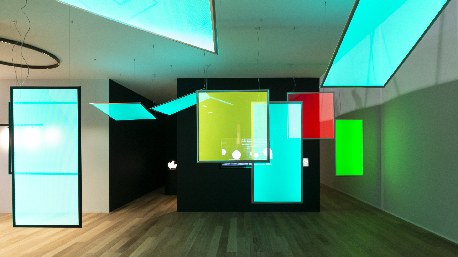Showroom Artemide con vivaci pannelli luminosi piatti in ciano, verde e rosso come luci a soffitto e a sospensione in un interno scuro.
