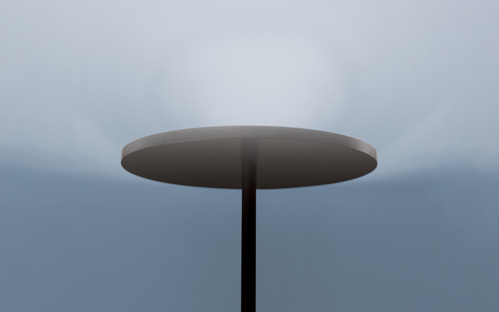 Lampada da terra Artemide con paralume a disco circolare scuro su sottile stelo nero, che emette una luce diffusa verso l'alto su cielo nuvoloso
