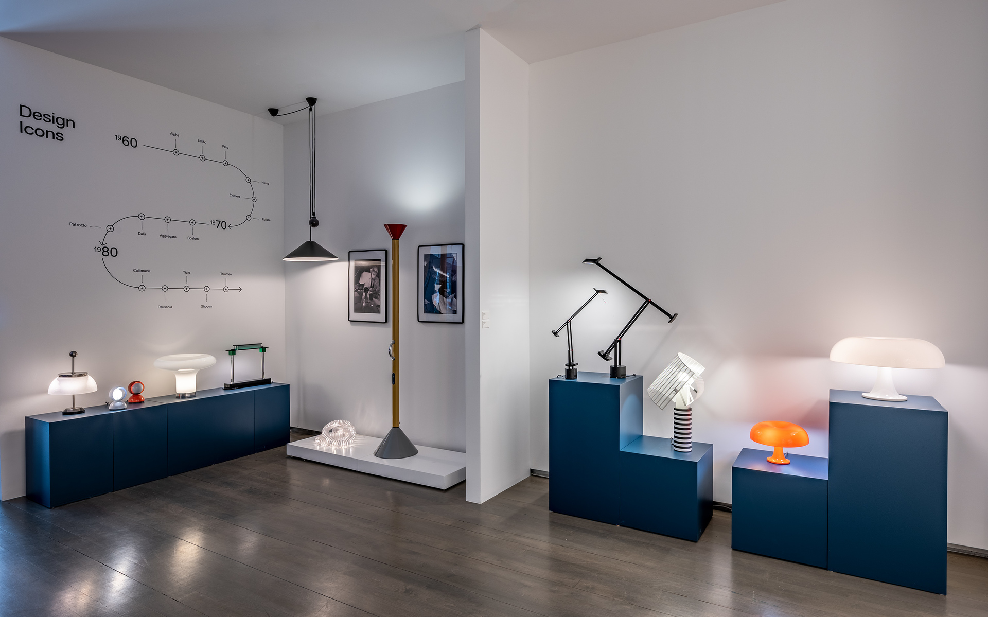 Mostra Artemide Design Icons con lampade iconiche su plinti blu, incluse lampade da tavolo, da terra e a sospensione di varie epoche.