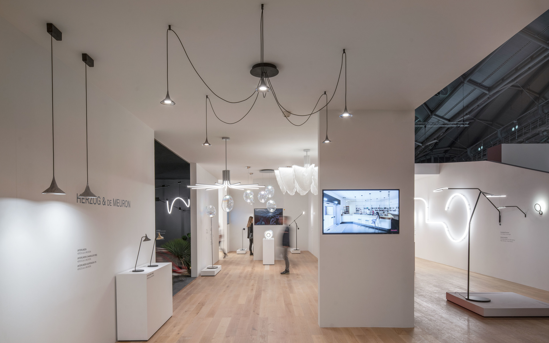 Artemide showroom displaying pendant, floor, and sculptural LED lights in a bright white exhibition space with wooden floors.
