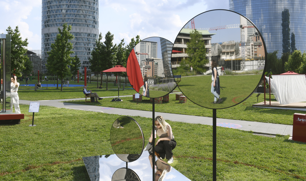 Installazione outdoor Artemide con specchi circolari su supporti in un parco urbano, che riflettono i visitatori e lo skyline della città.