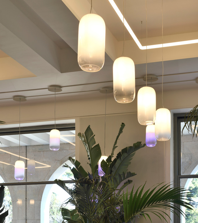 Lampade a sospensione Artemide Gople in vetro soffiato bianco con bagliore viola alla base, sospese su piante tropicali in un interno moderno