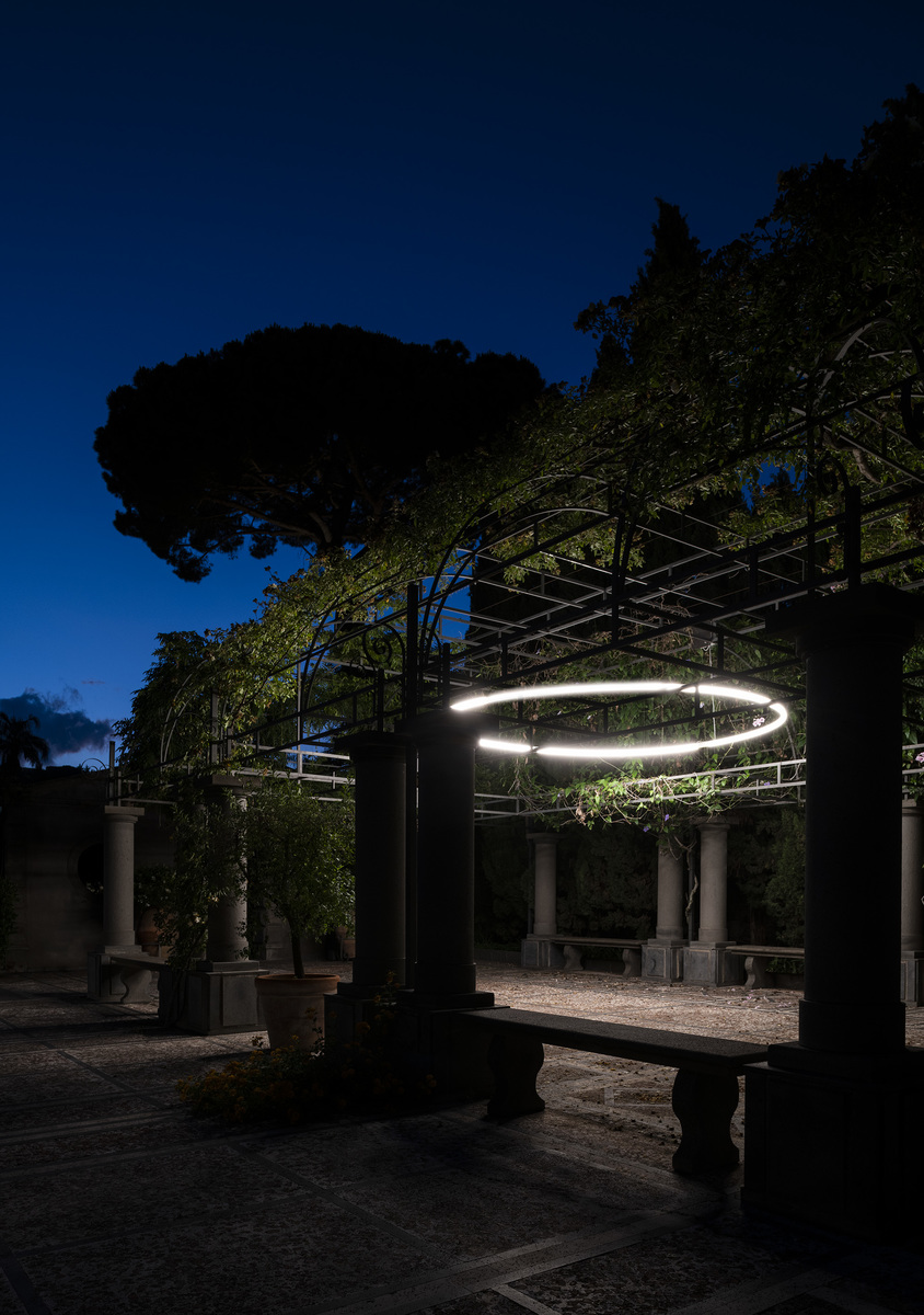 Artemide circular LED ring pendant light illuminating a classic Italian garden pergola with stone columns at dusk