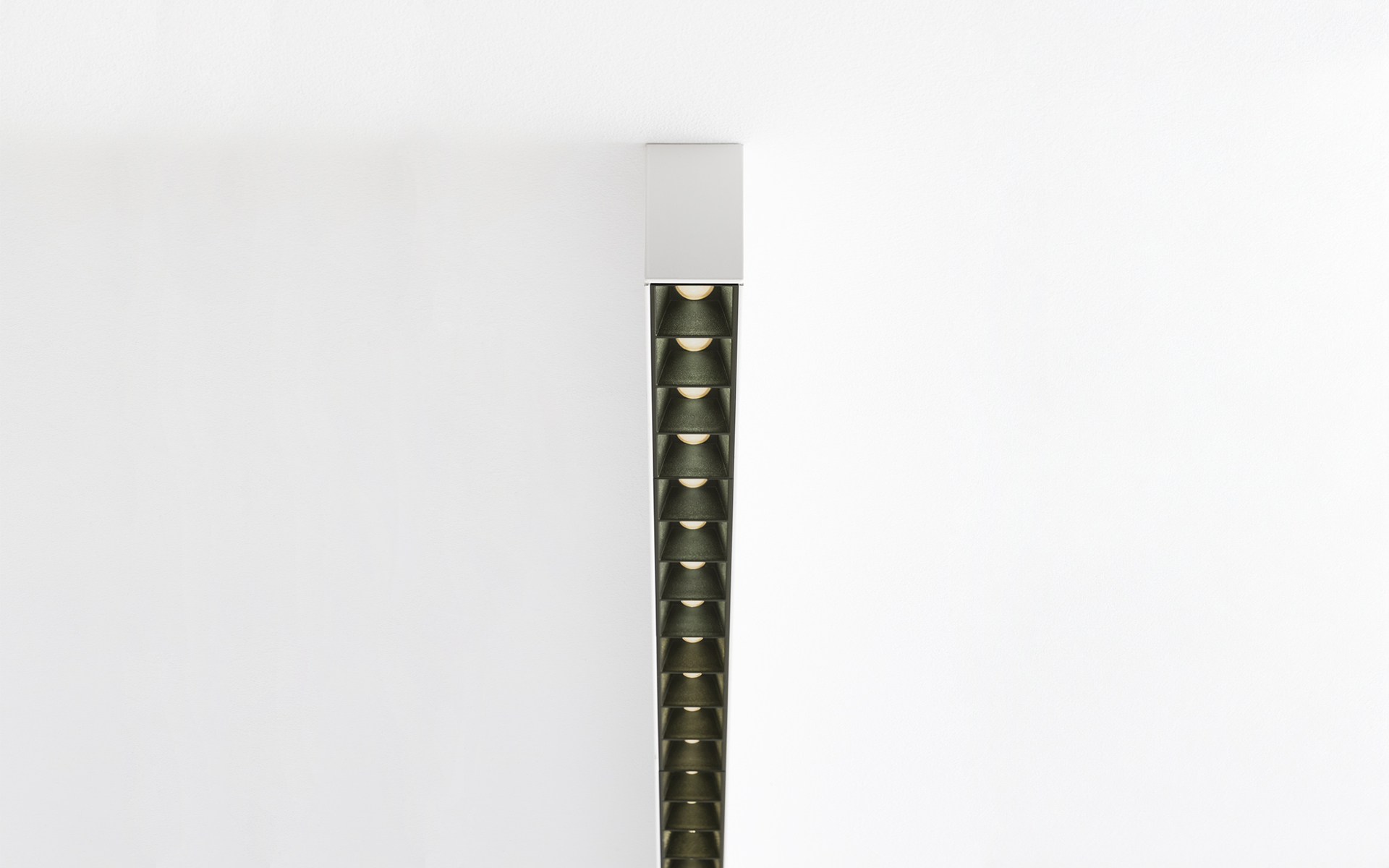 Apparecchio LED lineare verticale in bronzo scuro con celle a nido d'ape anti-abbagliamento, montato a soffitto, con luce direzionale verso il basso
