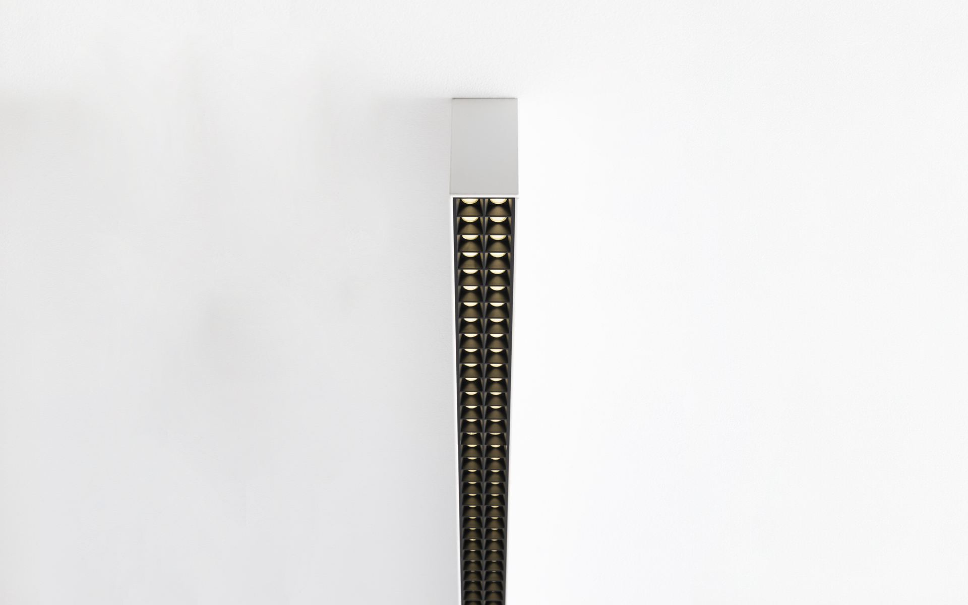 Lampada da parete verticale con corpo bianco sottile e doppia fila di piccole lenti LED dorate su striscia scura, montata a filo del muro