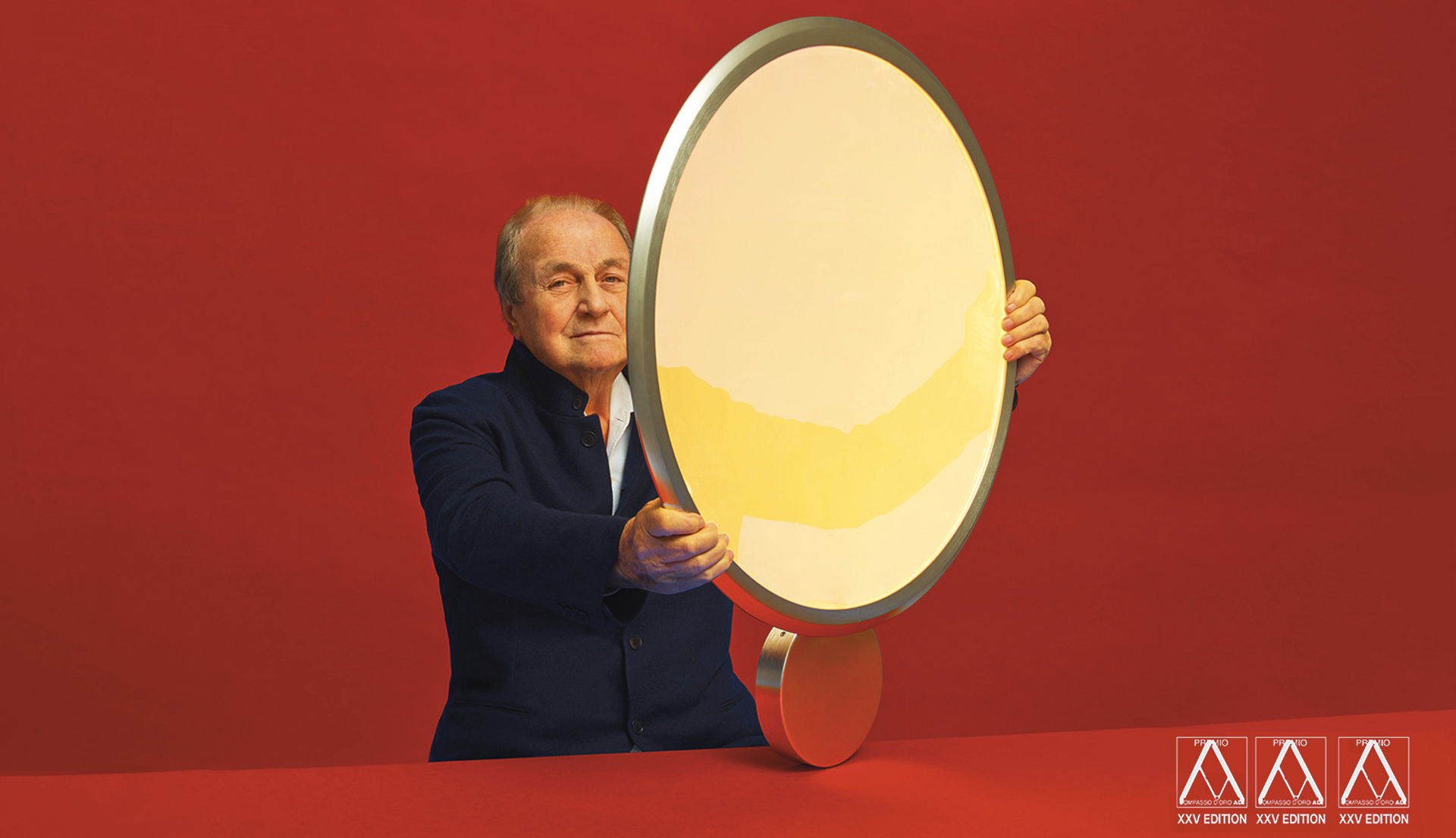 Designer che regge la lampada Artemide Fato, un luminaire LED ovale con bordo argentato e luce calda, su sfondo rosso.
