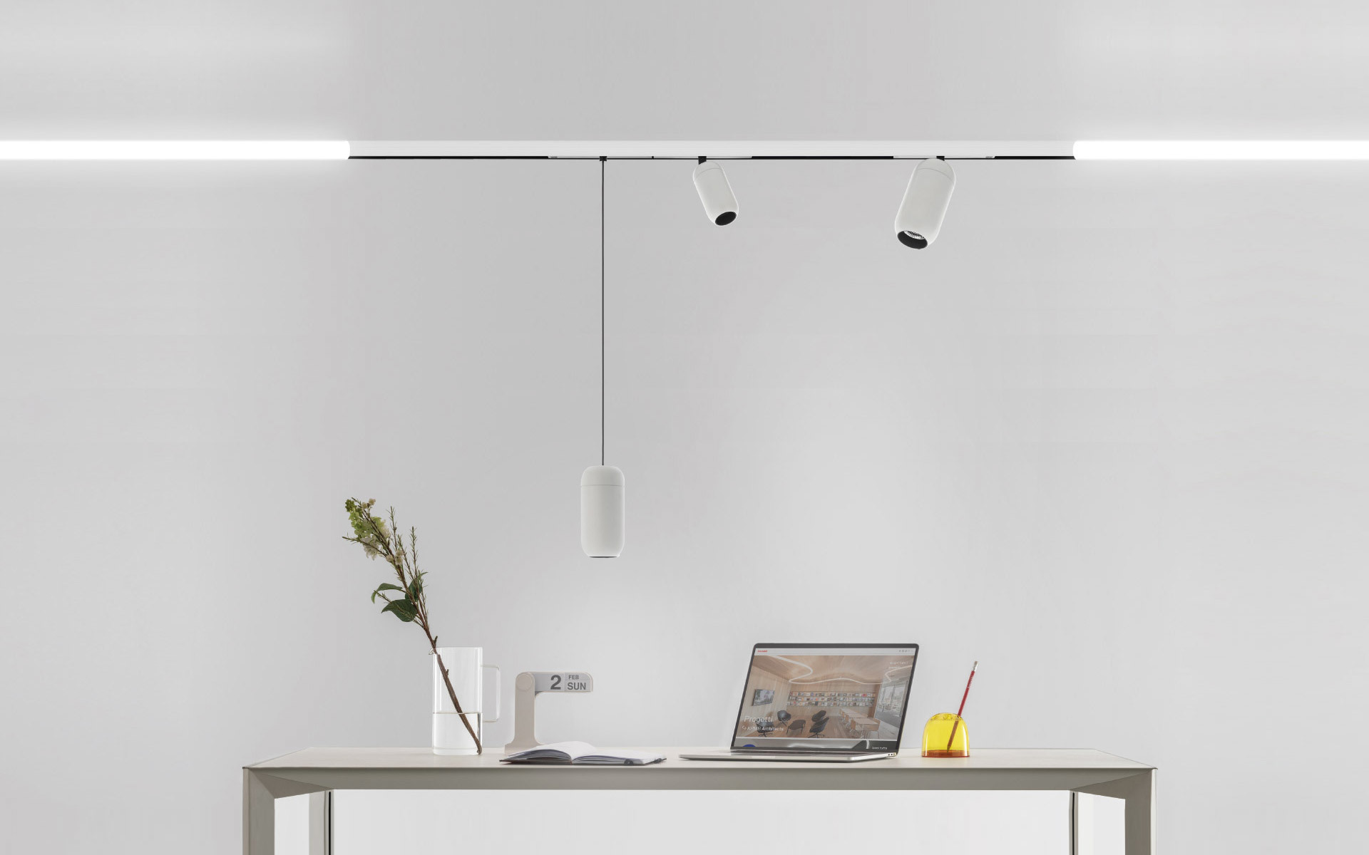Sistema di illuminazione su binario Artemide con barra LED lineare, due faretti orientabili e una lampada a sospensione cilindrica sopra una scrivania minimalista.