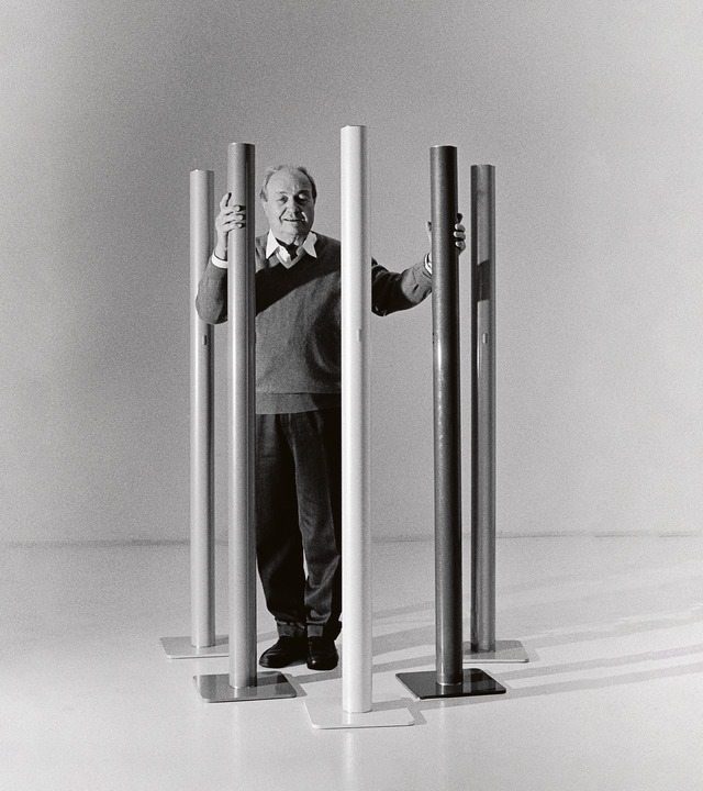 Immagine di Ernesto Gismondi fotografato a figura intera con le lampada Ilio attorno a lui.