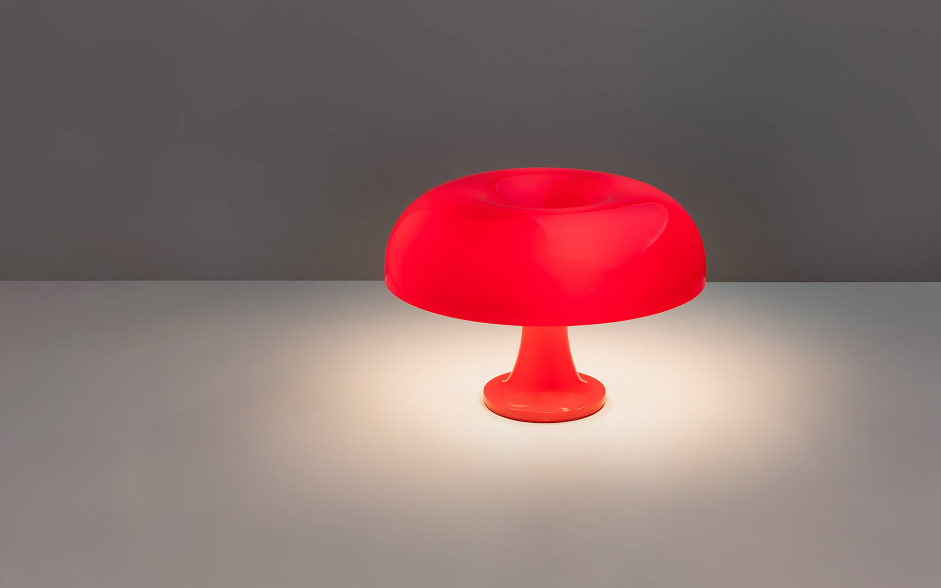 Lampada da tavolo Artemide Nessino rossa, diffusore a fungo su base slanciata, proietta luce calda su una superficie