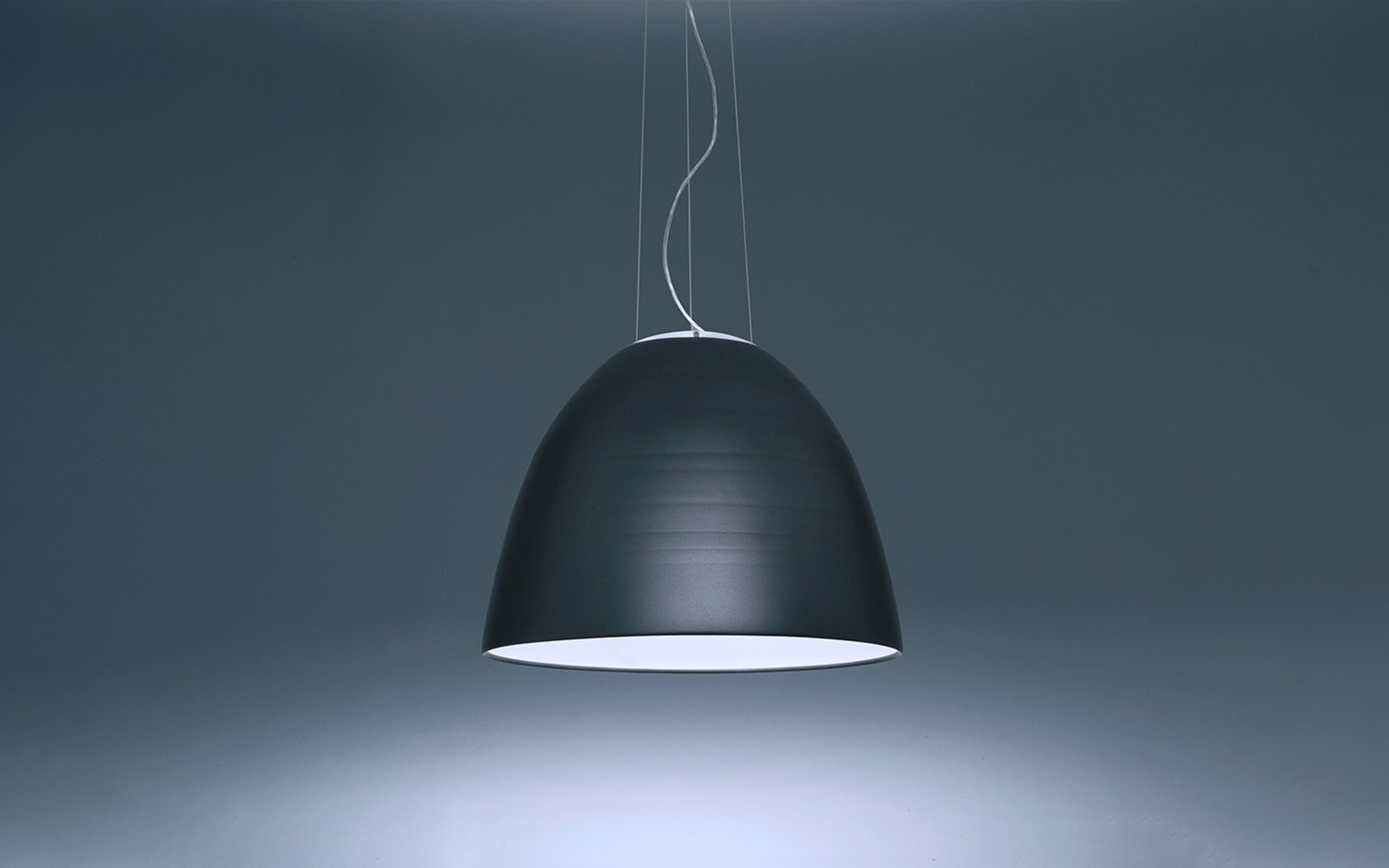 Lampada a sospensione Artemide a cupola antracite scuro con diffusore interno bianco, sospesa da sottili cavi, con luce orientata verso il basso.