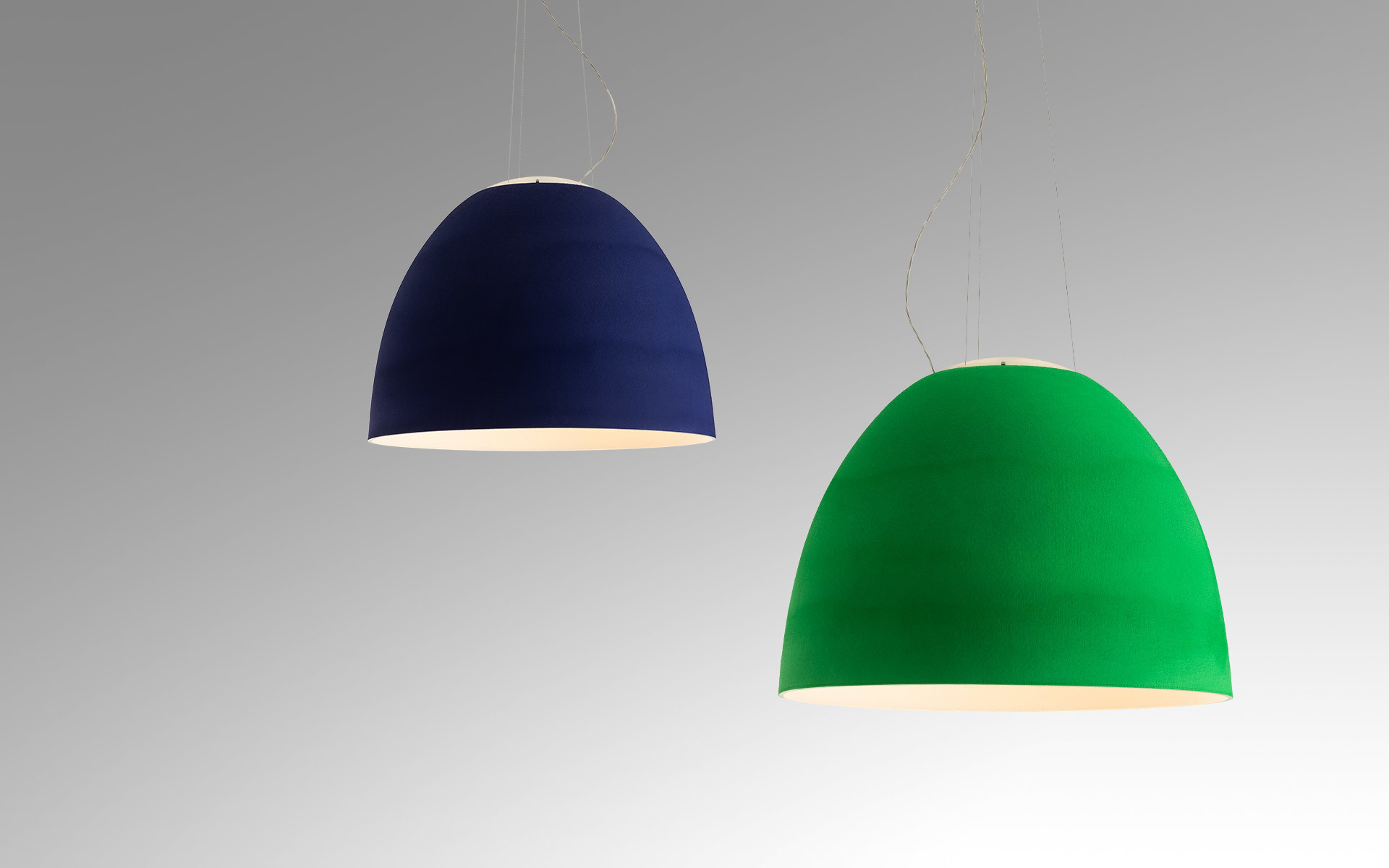 Due lampade a sospensione Artemide con paralumi a campana: sinistra blu intenso, destra verde vivace, che emettono luce calda verso il basso.