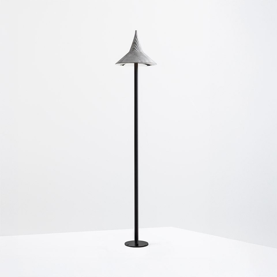 Lampada da terra Artemide Unterlinden Outdoor: alto fusto nero con base rotonda, sormontato da un paralume conico grigio testurizzato rivolto verso l'alto