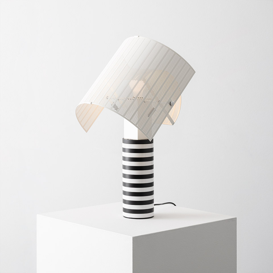 Lampada da tavolo Artemide Shogun con base cilindrica a strisce bianche e nere e paralume bianco nervato inclinato, su piedistallo bianco
