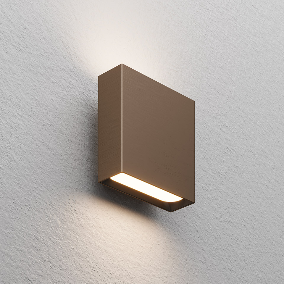 Applique Agathe di Artemide: corpo quadrato compatto color bronzo con striscia LED inferiore che emette luce calda verso l'alto e il basso