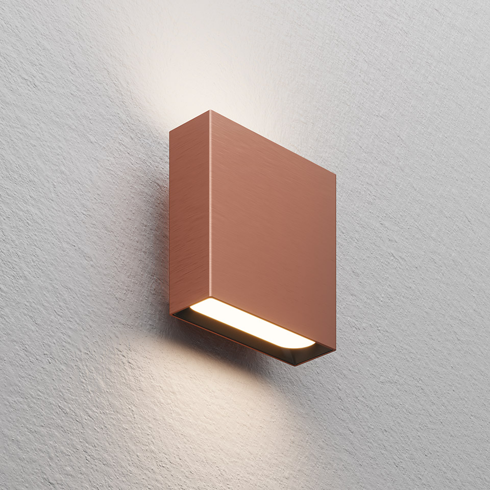 Lampada da parete Artemide Agathe finitura rame, corpo quadrato che emette luce bianca calda verso il basso e l'alto su parete texturizzata