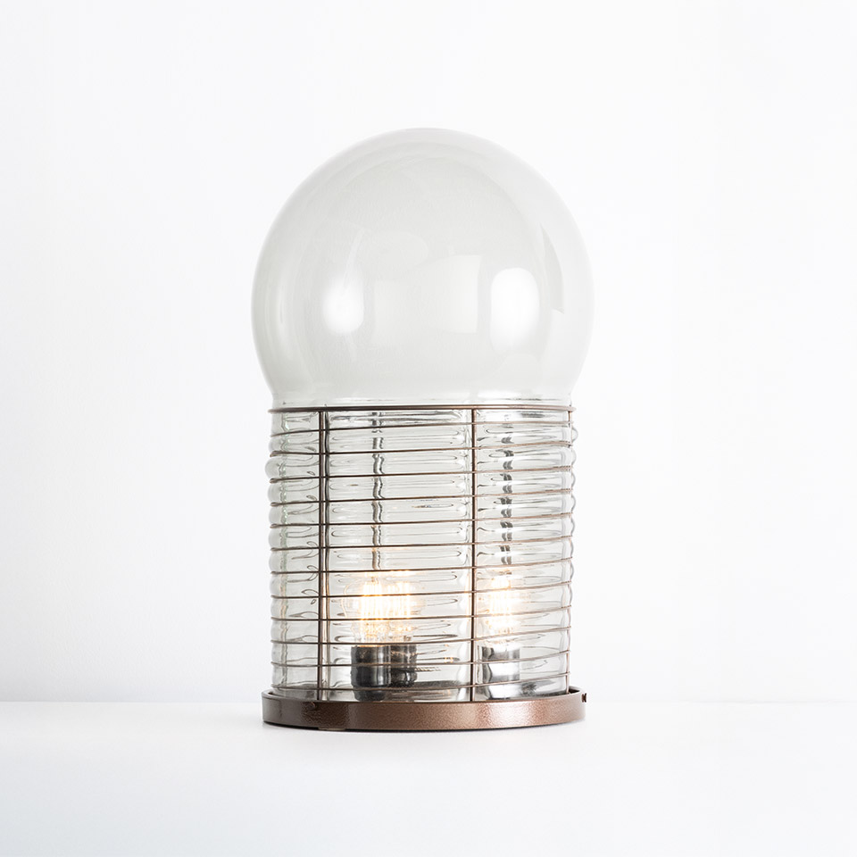 Lampada da tavolo Artemide Alcinoo: cupola in vetro trasparente su corpo cilindrico costolato con base in bronzo metallico e bulbo a filamento visibile