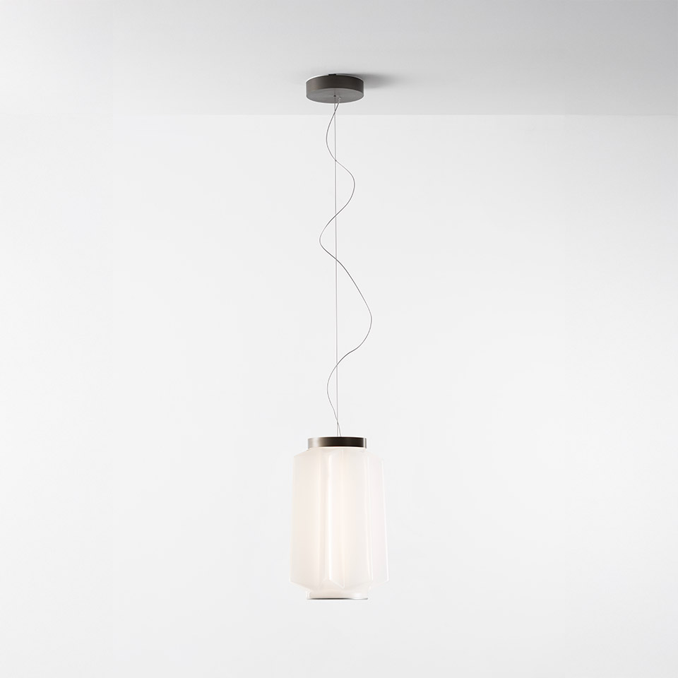 Lampada a sospensione Artemide Auralia: diffusore cilindrico in vetro opalino con calotta superiore in metallo scuro, sospesa da un cavo ondulato a un rosone a soffitto