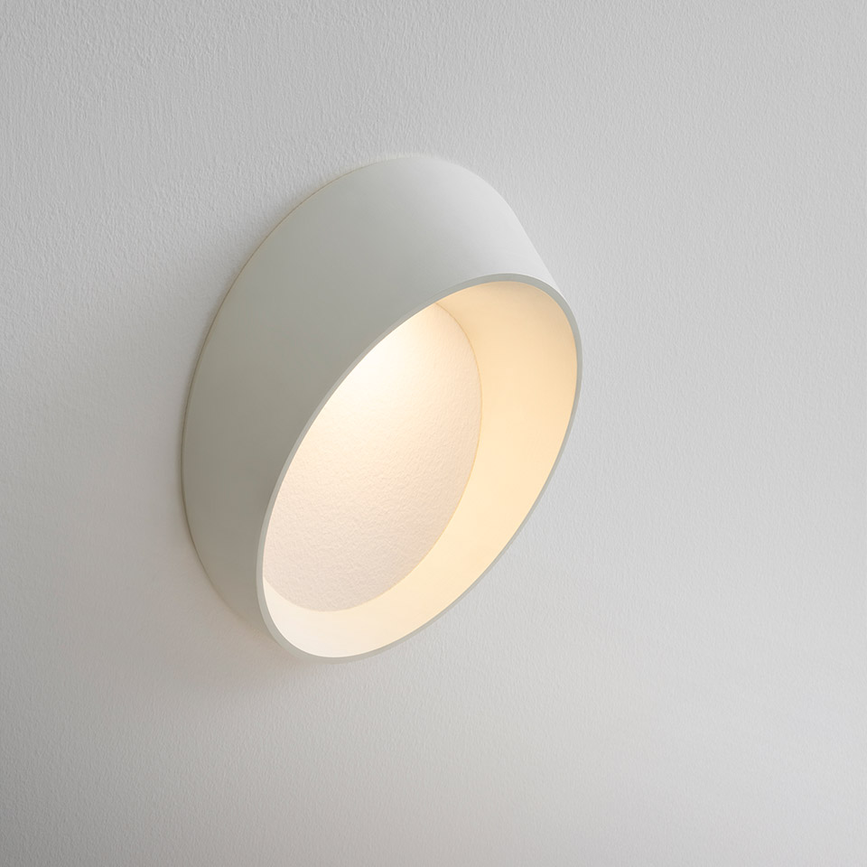 Applique Artemide Cleomede: paralume cilindrico bianco inclinato con luce LED calda, montato a filo su parete bianca