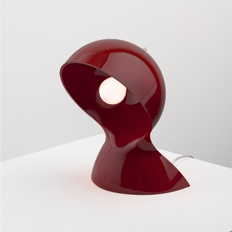 Lampada da tavolo Artemide Dalù in rosso scuro lucido, con forma a conchiglia curva scultorea e bulbo a vista, su superficie bianca