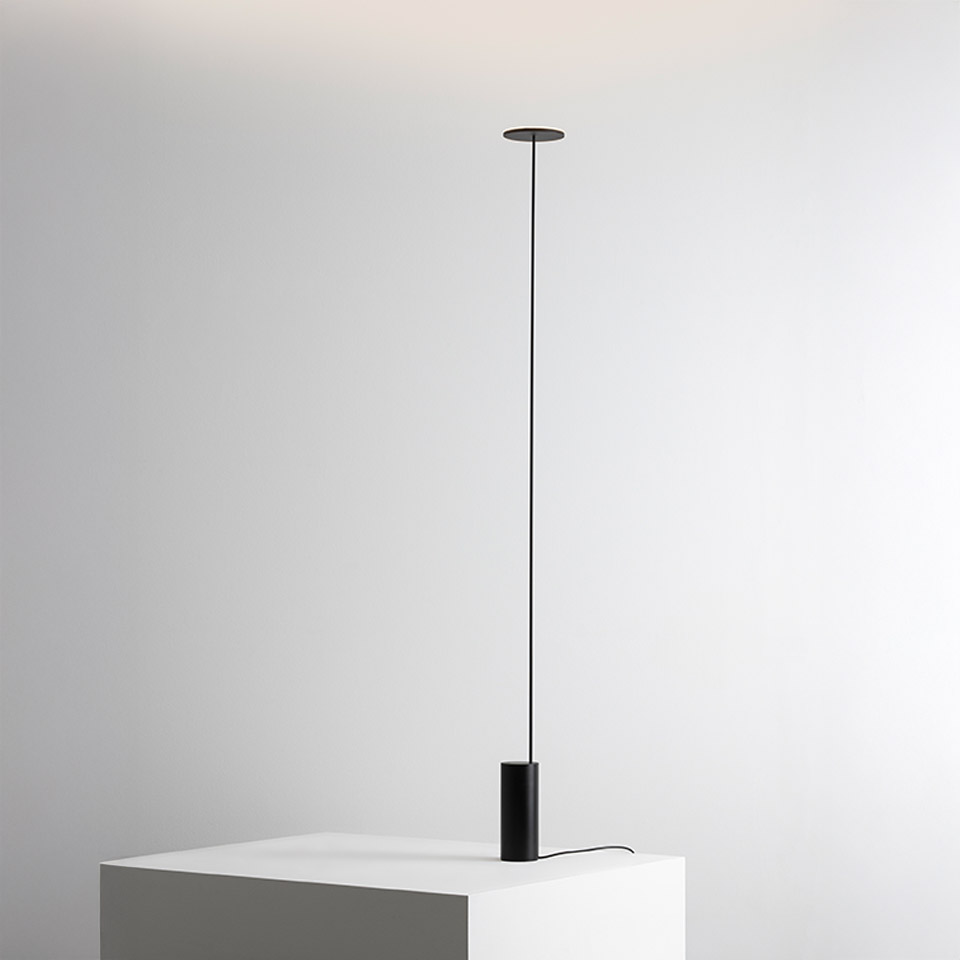 Lampada da terra Artemide Helgoland: stelo nero ultrasottile che collega il rosone a soffitto alla base cilindrica su superficie bianca