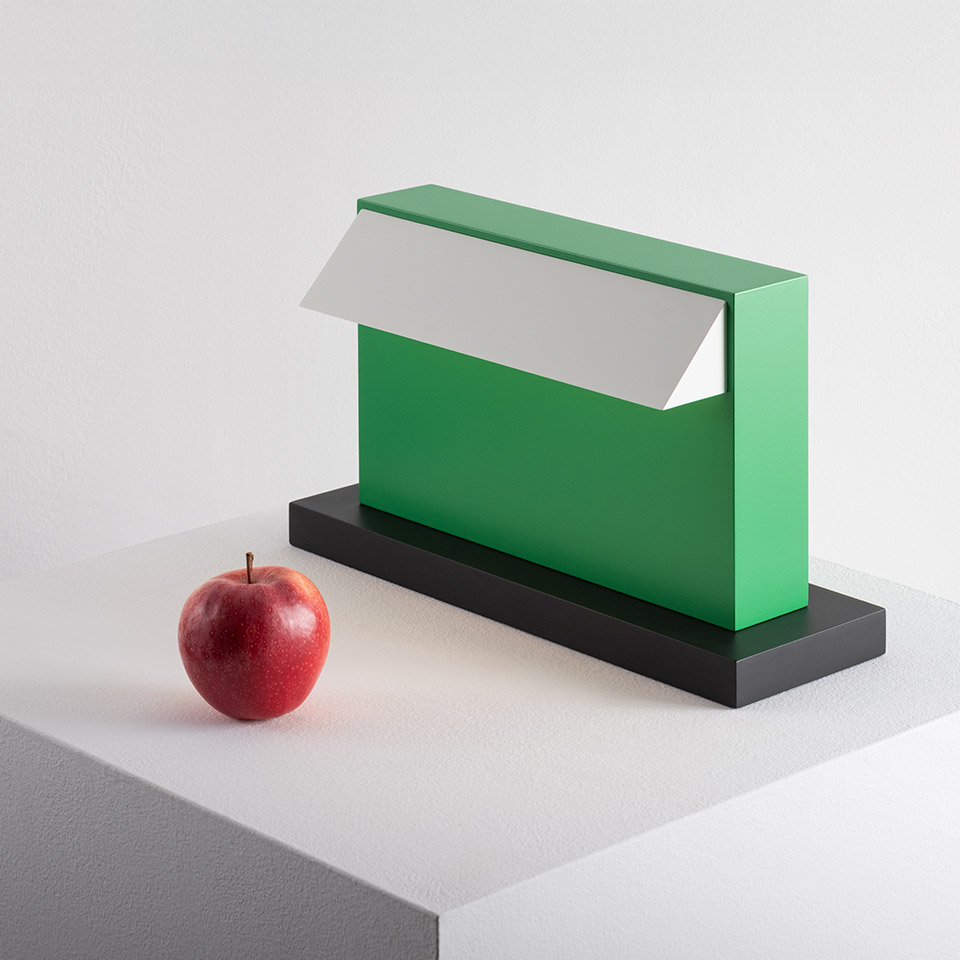 Lampada da tavolo Artemide Hera verde con riflettore bianco su base nera, mostrata accanto a una mela rossa per scala