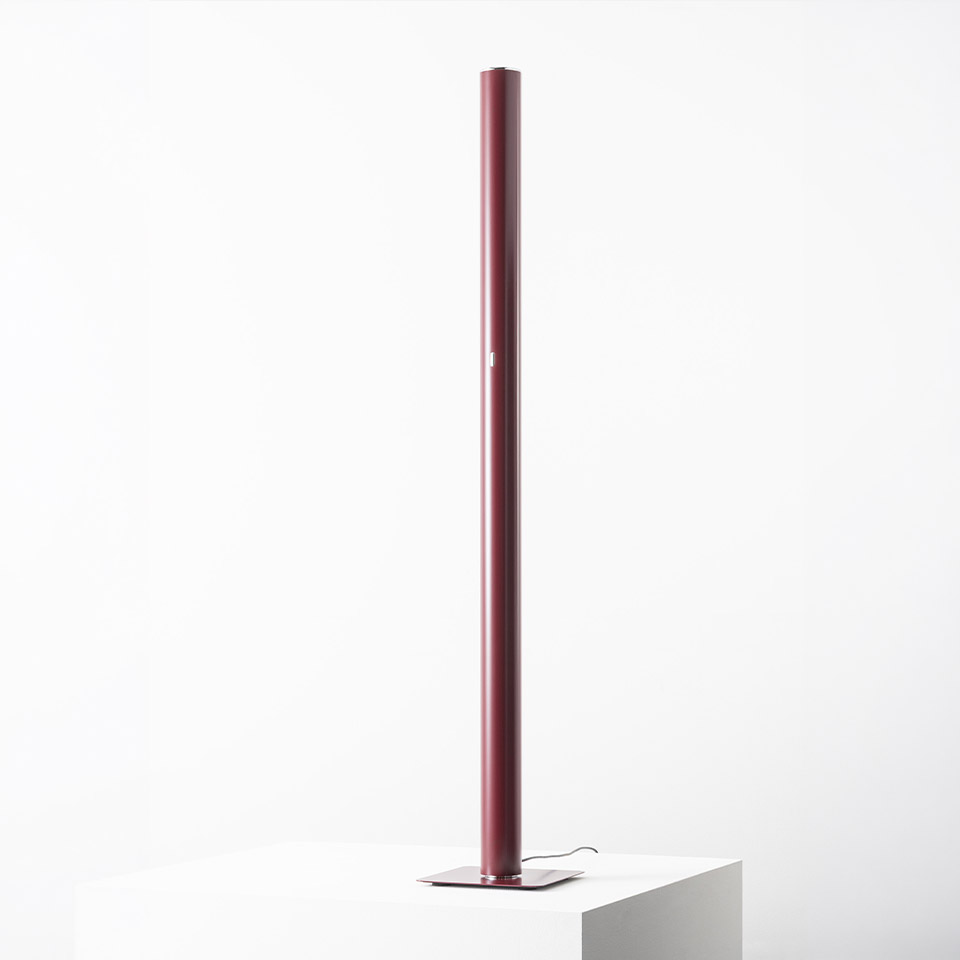 Lampada da terra Artemide Ilio: alto tubo cilindrico bordeaux su base quadrata piatta, emette luce ambientale indiretta