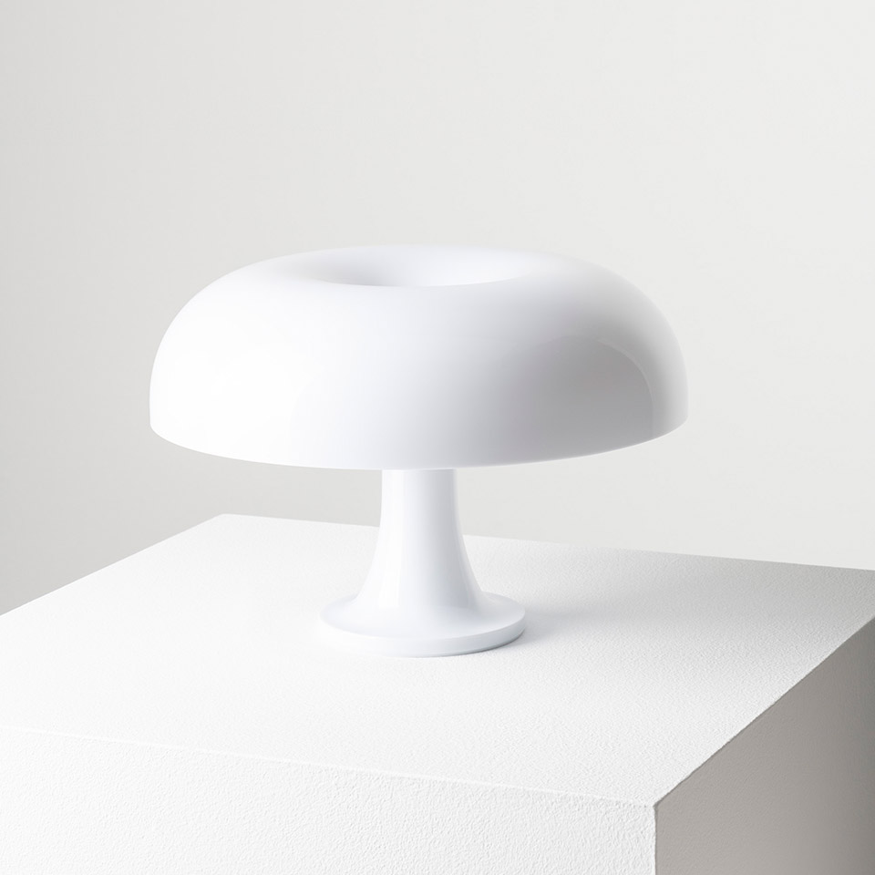 Lampada da tavolo Artemide Nessino bianca, con diffusore rotondo a forma di fungo su base a piedistallo, che emette una luce d'ambiente soffusa