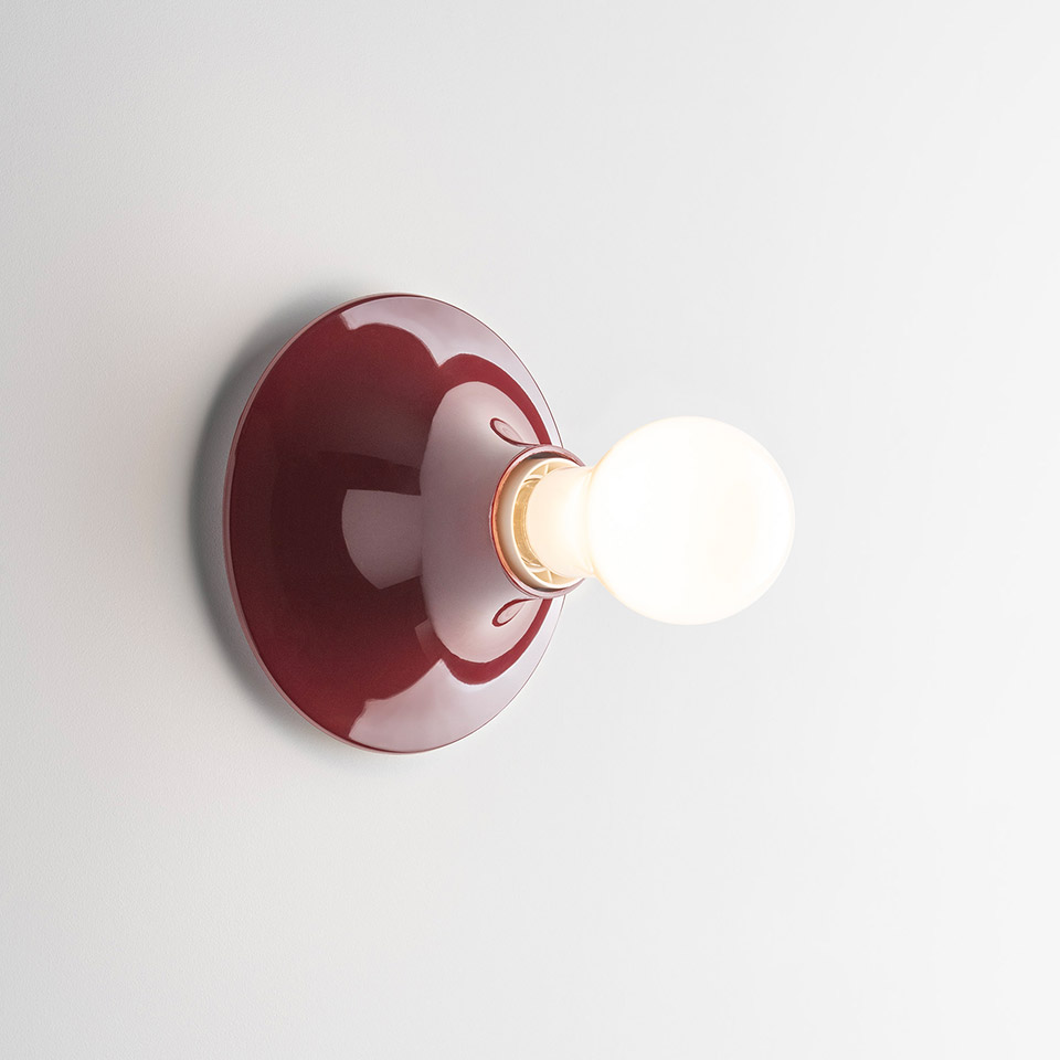 Artemide Teti wall lamp with glossy burgundy round base and exposed spherical frosted bulb mounted on white wall